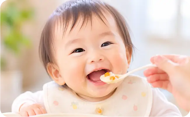 スプーンで離乳食を食べる笑顔の赤ちゃん