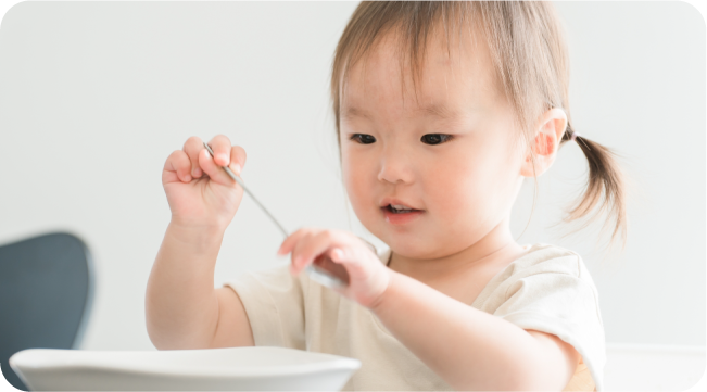 スプーンを手に食事をする幼い子ども